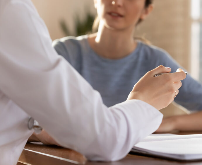 Close up young female general practitioner gesturing, communicating with patient at checkup meeting in clinic office. Focused doctor explaining medical insurance benefits or health treatment protocol.