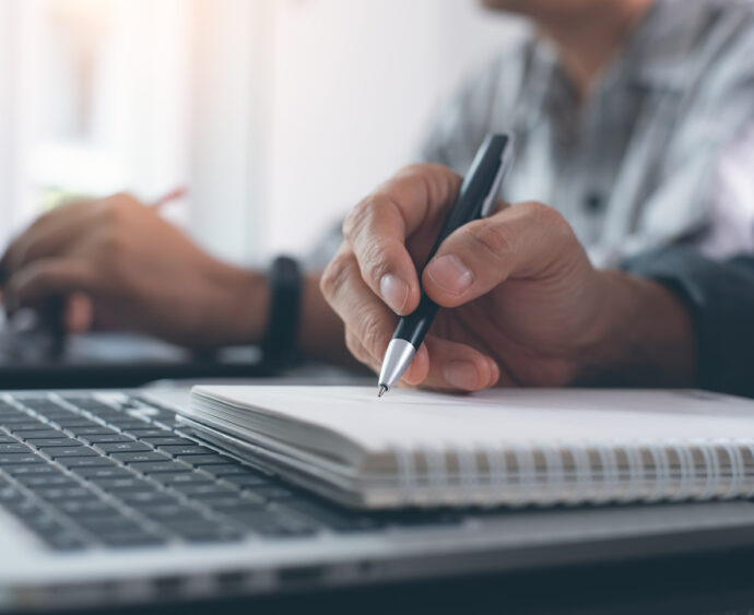 Elearning, online working concept. Business man working on laptop computer, searching and taking note on paper notebook with pen. Students attending course online class
